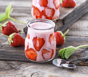 成熟的红色草莓和两个玻璃罐的冰沙在一个灰色的木桌上, 关闭