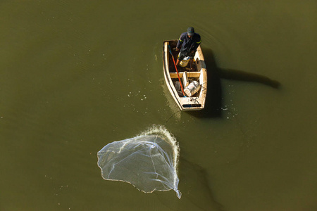 渔夫铸造网行动钓鱼从小船入河泻湖水顶上的相片