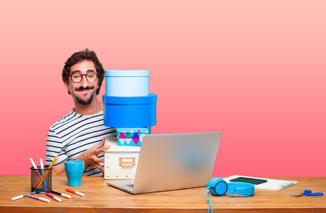 年轻疯狂的平面设计师在一张办公桌上与笔记本电脑和礼品盒的概念照片