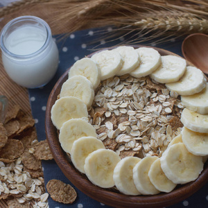 木碗有机玉米片和燕麦片与香蕉, 牛奶在玻璃瓶中, 选择性聚焦。营养早餐, 生食配料, 健康生活方式