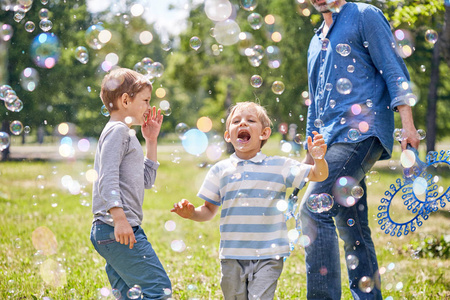 在绿色的公共公园举行儿童派对时, 可爱的小男孩试图用嘴捕捉肥皂泡的肖像
