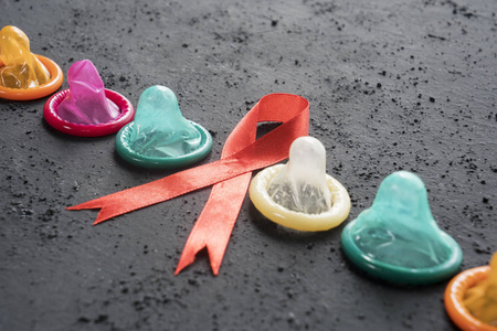 在黑色桌子上用彩色避孕套关闭红色丝带。世界艾滋病日概念