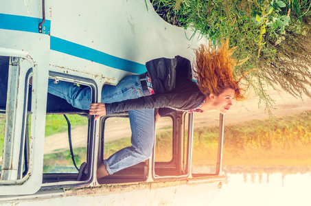 年轻女孩红色的头发坐在打破的公共汽车窗口的边缘