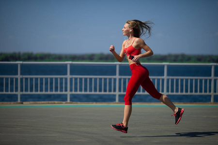 年轻的健身妇女夏天在海岸上奔跑。健康生活方式的概念