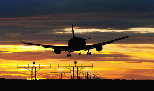 剪影飞机在着陆期间在日落天空在背景。飞机抵达机场