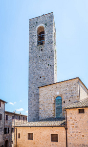 垂直照片与高石塔。塔位于联合国教科文组织古镇圣吉米尼亚诺。钟在塔顶。周围有几栋楼。天空是蓝色和清澈的