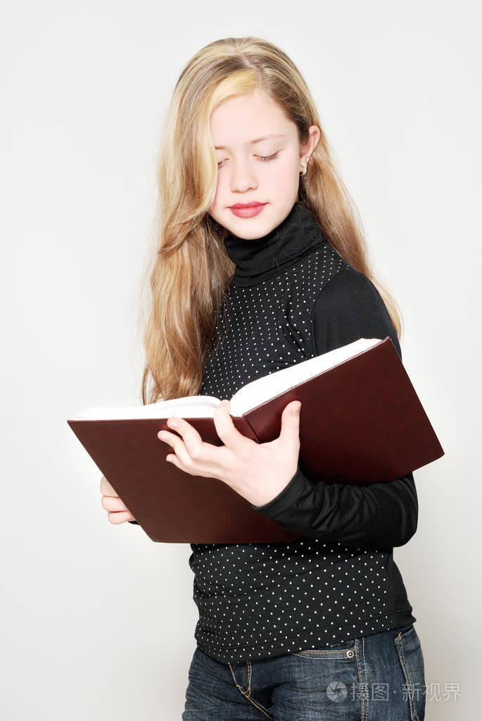 微笑的金发女孩拿着书站在光的背景下