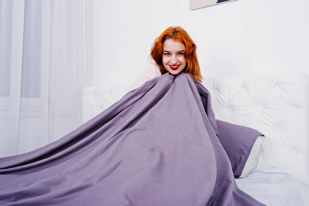 一个迷人的红发女孩的肖像躺在床上, 覆盖自己的紫色毯子