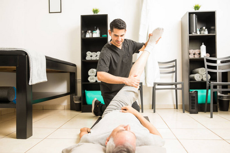 青年理疗师帮助成熟男子腿部锻炼在康复诊所中的应用