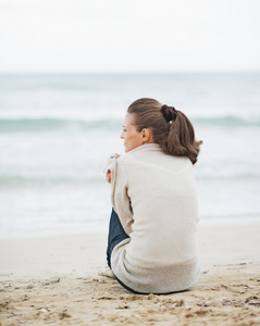 年轻女子坐在海滩上的毛衣环绕