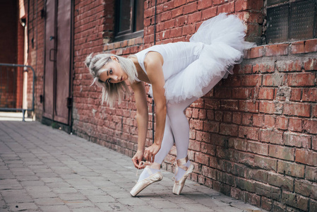美丽的年轻芭蕾舞女演员倚在砖墙和绑尖鞋