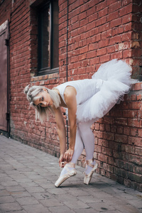 有吸引力的年轻芭蕾舞女演员倚在砖墙和绑尖鞋