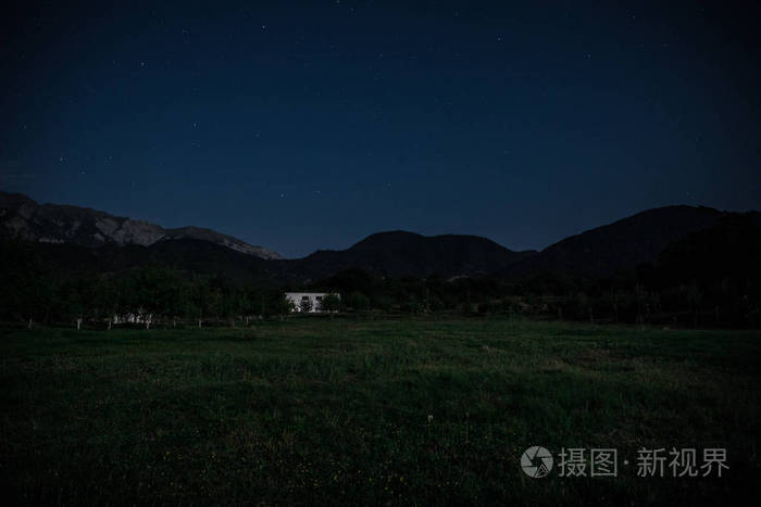 晚上在森林里建筑的山夜风景与月亮或老式乡下房子在晚上与云彩和星