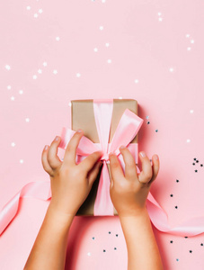 在粉红色背景的孩子手拿着美丽的礼物盒