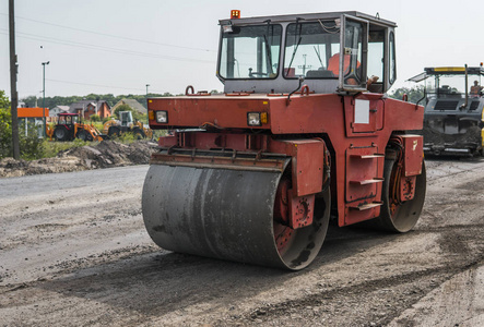 在沥青路面工程中进行道路修复的橙色重型振动压路机。在新的道路建设工地工作。修复