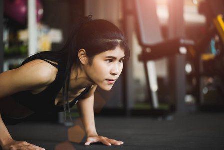 亚洲年轻女子在健身房做俯卧撑。肌肉女做俯卧撑。运动和健康的生活方式概念