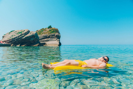 年轻男子在黄色充气床垫在清澈透明的水。暑假概念