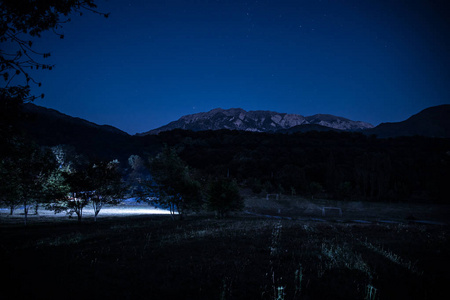 美丽的夜晚景观与繁星夜山和森林。夜森林与绿色草甸和山在明亮的繁星夜或银河看法