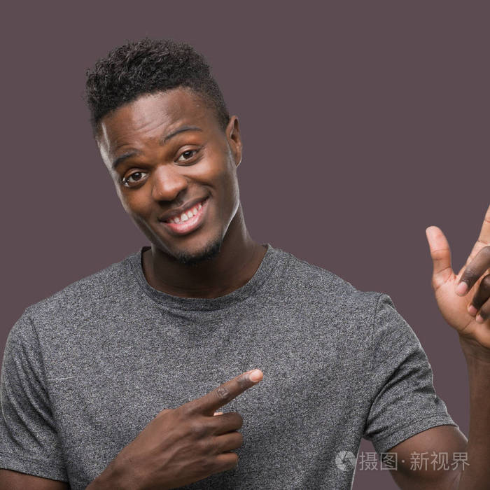 年轻的非洲裔美国人穿着灰色t恤微笑着看着相机指着两只手和手指的