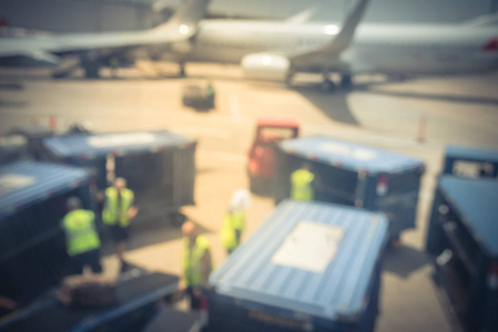 模糊的机场乘员组与传送带和行李卡车卸载行李到达在晴朗的天在达拉斯, 得克萨斯, 美国