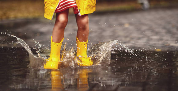秋天的沃尔玛在水坑中的黄色橡胶靴快乐的孩子