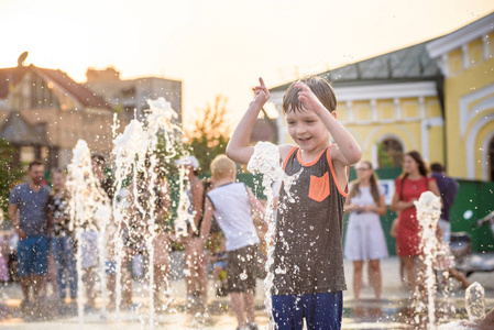 兴奋的男孩在水射流之间的乐趣, 在喷泉。夏天在城市。孩子用手打水开心地笑着脸。生态学概念