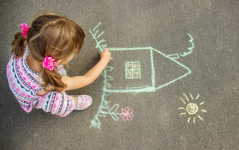 孩子用粉笔在沥青上画房子。选择性对焦。画