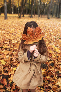 六岁女孩躲在秋天的大枫叶后面