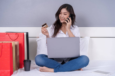 幸福的女人在她的床网上购物与智能手机和信用卡
