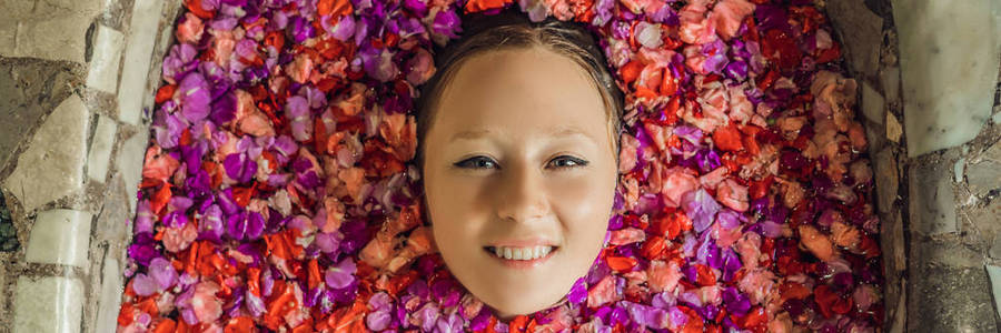 迷人的妇女的脸在浴与粉红色的热带花的花瓣