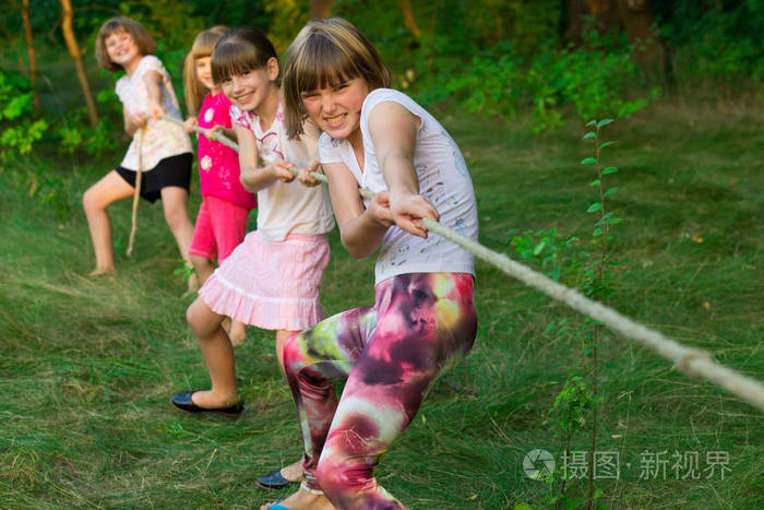 一群快乐的孩子在草地上玩拔河比赛孩子们在公园里拉绳子夏令营乐趣