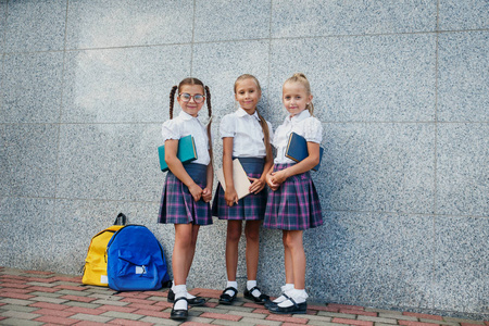 小学生的小学。女孩有背包和书籍在户外建筑附近。课程开始。秋天的第一天