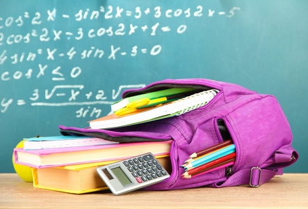 紫色背包和学校用品木制的桌子上绿色的桌子背景上