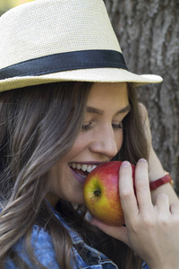 美丽的微笑的年轻妇女的画像与帽子吃苹果在享用