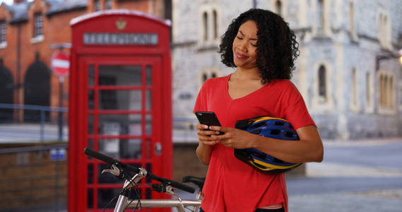 在英国自行车旅游中微笑的黑人妇女微笑着在手机上发短信