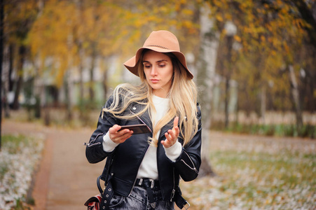 时尚秋画像年轻快乐的女人走在秋季公园的帽子和皮革夹克户外