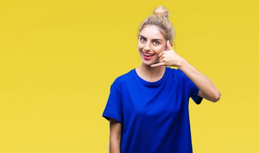 年轻美丽的金发碧眼的女人穿蓝色 t恤衫在孤立的背景微笑做电话手势用手和手指喜欢说话的电话。沟通概念