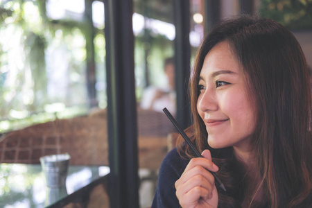 一个美丽的亚洲女人的特写肖像在现代咖啡馆里坐着笑脸, 同时思考商业和学习