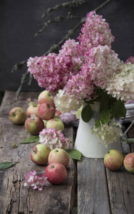 五颜六色的丁香花在白色罐头和成熟苹果在木背景
