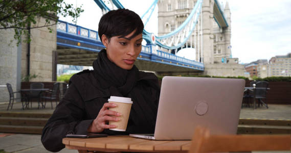 伦敦塔桥附近的黑人女性在户外的笔记本电脑上观看视频