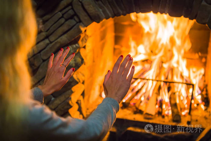 金发碧眼的女孩在壁炉里的炉火旁温暖着她的双手壁炉附近舒适的冬日