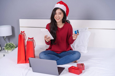 快乐的妇女网上购物的圣诞礼物与数字平板电脑和信用卡在床上