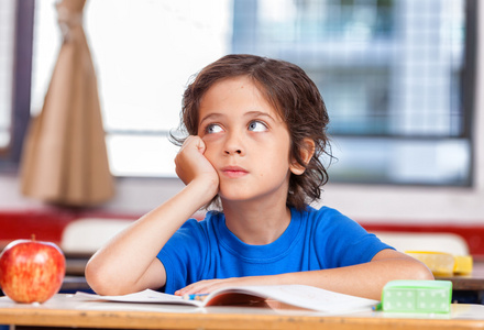 小学孩子坐在他办公桌前的答案的思考照片