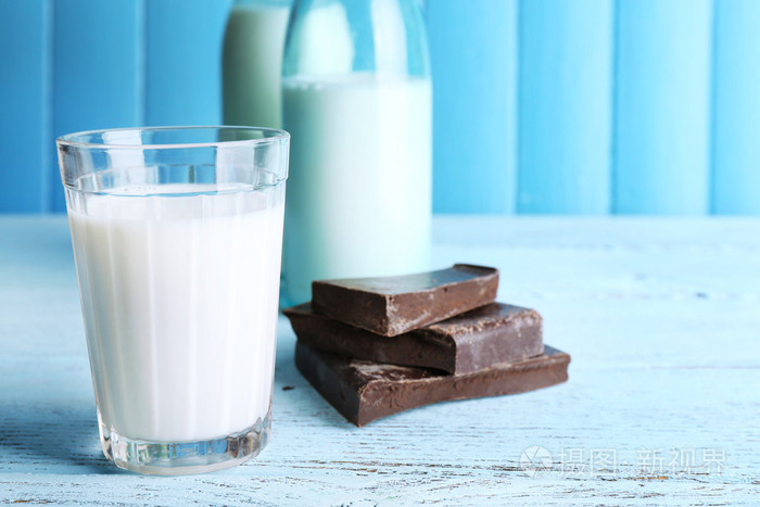 玻璃和瓶牛奶与巧克力块彩色木板背景
