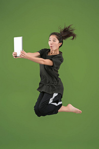 年轻妇女的形象在绿色背景下使用膝上型电脑或 tablet 小工具跳跃