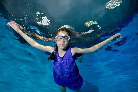 一个小女孩的辫子从事体育运动, 游泳水下在泳池中的紫色泳装, 看着相机。肖像。底部视图。图像的水平方向