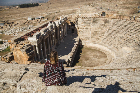 在土耳其古代希拉波利斯的圆形剧场里, 她的背景下的女性旅行者在露天剧场里看着惊人的风景