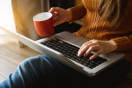 womman 使用笔记本电脑和打字在笔记本电脑和持有咖啡杯在咖啡厅, 家庭办公室在上午光