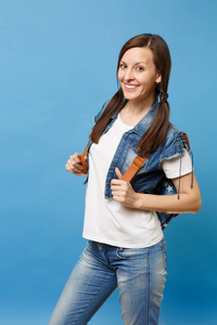 年轻迷人的微笑的黑发女学生的肖像白色 t恤衫, 牛仔服装与背包站在蓝色背景孤立。大学教育。复制广告空间