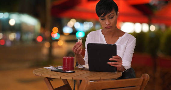 非洲女性在餐厅外用餐, 同时在平板电脑上阅读